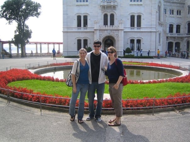three people standing in front of a manicured garden and a castle