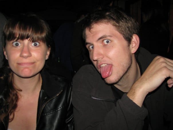 woman in a leather jacket sitting next to man sticking his tongue out