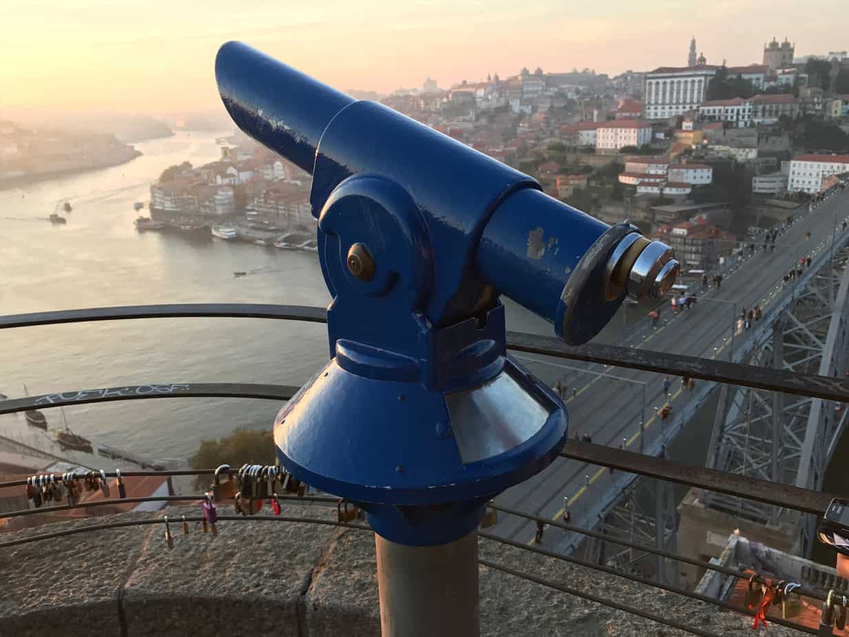 telescope in foreground of city and river view at sunset