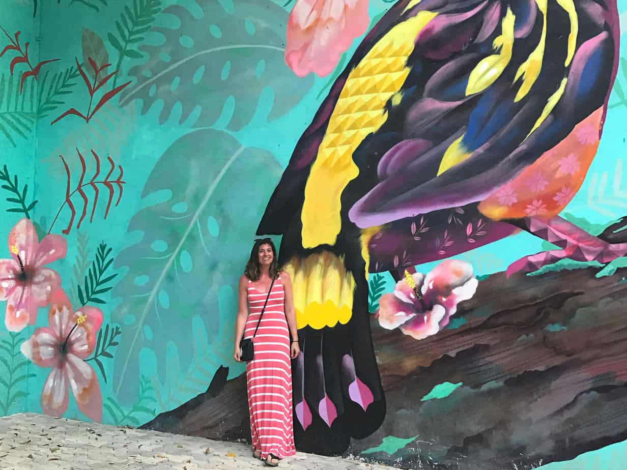 woman in pink striped dress standing in front of colorful mural