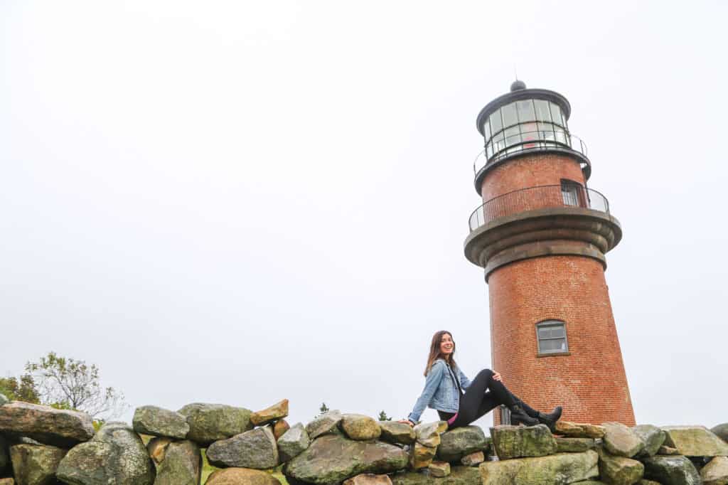 woman sitting on rock wall in front of brick lighthouse on a foggy day
