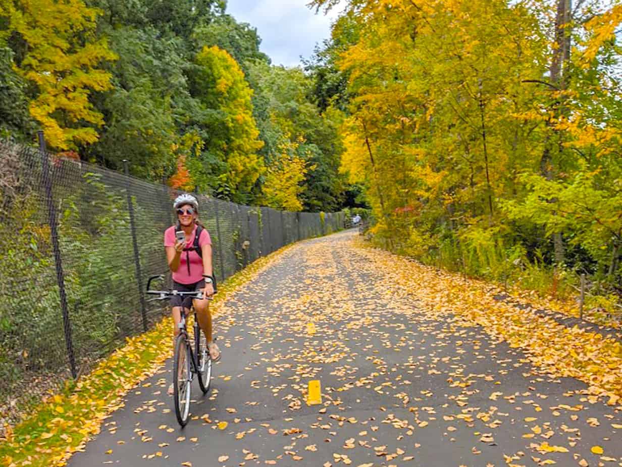 woman taking cell phone picture on a bike surrounded by yellow leaves